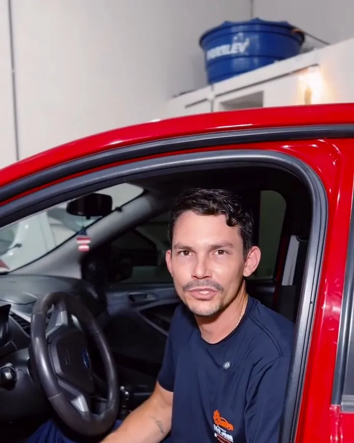 Mecânico sentado no banco do motorista de um carro vermelho na oficina